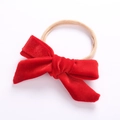Detail view of a beige nylon headband featuring a soft red velvet bow for infants - Red