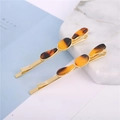 Detail of two golden hair clips with amber oval resin stones on a marble background - Wave Gold
