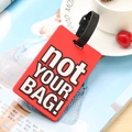 Red PVC luggage tag with 'not YOUR BAG!' text and black strap on a desk setting - Not Your Bag / Red