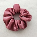 Detail of soft dusty pink satin scrunchie with glossy pleated texture on a fabric surface - Dark Pink