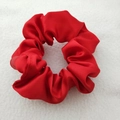 Close-up of a red satin scrunchie with soft silk texture on a white plush surface - Red