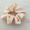 Detail view of champagne satin fabric texture and soft luster on a high-elastic scrunchie - Beige