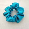 Close-up of a turquoise satin scrunchie showing glossy fabric texture and soft folds - Turquoise