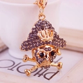 Golden pirate skull keychain with grey rhinestones and crown hat on crossbones - Gray