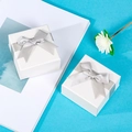 Detailed view of two white square jewelry gift boxes with silver ribbons on a blue surface - Bow with Handbag Set