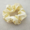 Close-up of yellow satin silk scrunchie with soft pleated texture on gray felt background - Yellow