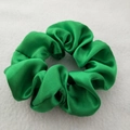 Close-up of a green satin scrunchie with glossy pleated texture on a white felt surface - Fruit Green