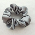 Close-up of a grey satin scrunchie showing glossy texture and soft silk-like fabric folds - Gray