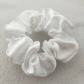 Close-up of a white satin scrunchie featuring smooth glossy texture and high elasticity - White