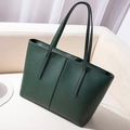Minimalist large dark green leather tote bag with long shoulder straps on a sofa - Green