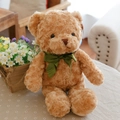 Brown teddy bear plush toy wearing a green ribbon bow tie sitting on a cozy sofa - Tan Bow-tie Bear