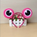 Pink plush frog headband with large cartoon eyes on a decorative white fence - Rose Red Frog