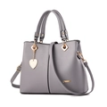 Elegante graue Damen-Handtasche aus Leder mit goldenem Herzanhänger und Tragegriffen - Hellgrau