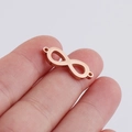 Vue macro d'un pendentif infini en or rose sur le bout d'un doigt pour bijoux DIY - Or rose