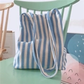 Dettaglio della borsa tote in tela a righe bianche e blu su sedia di legno - Azzurro