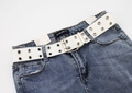 Detail of white double grommet canvas belt styled on blue denim jeans waist - White