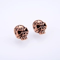 Detailed macro view of vintage bronze skull stud earrings with aged metal texture - Antique Rose Gold