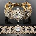 Goldenes Brautarmband mit breitem Banddesign und funkelnden ovalen weißen Kristallen - Gold