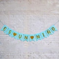 Spanish 'ES UN NIÑO' light blue party banner with gold letters on white brick wall - Blue (It's a Boy)