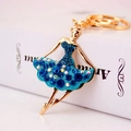 Golden alloy ballet girl keychain with blue crystals on white vintage book background - Blue