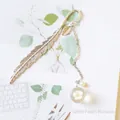 Detailed silver feather bookmark featuring a clear glass bead with dried white peach blossom - White Peach Blossom