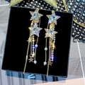 Detail von goldenen Stern-Ohrhängern mit Strass und Perlen auf einer schwarzen Box - Stern-Quasten-Stil / Weiß