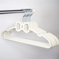 Close-up of cream white bow-shaped non-slip plastic hangers hanging on a metal rod - White Bow Shape