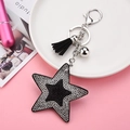 Détail macro du porte-clés étoile orné de strass bicolores et pompon élégant - Noir/Zircone Blanc