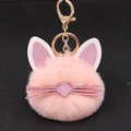Close-up of pink plush cat keychain with gold keyring on black background - Pink