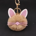 Cute brown plush kitten keychain with pink glitter ears and gold metal clasp on black background - Khaki