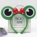 Green plush frog headband featuring large eyes and a red polka dot bow for kids - Green Frog with Small Bowknot