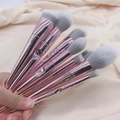 Gros plan de 10 pinceaux de maquillage or rose avec fibres gris-blanc sur tissu beige - 10 Pinceaux à Manche Rose + Sac OPP