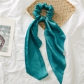 Teal satin scrunchie with long ribbons on a decorative woven mat and white background - Lake Blue
