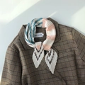Dettaglio di un foulard in seta plissettato a righe abbinato a un blazer a quadri marrone - Rosa