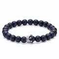 Detalle de una pulsera de cuentas negras mates con un dije de corona plateada y circonitas - Piedra mate