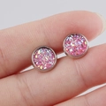 Close-up of 8mm round pink glitter stud earrings held between fingers for size reference - Pink (1)