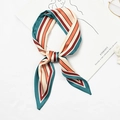 Striped silk scarf in green and orange tied in a bow on a minimalist white desk - Wide and Narrow Stripes Indigo Edge