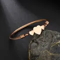Close-up of rose gold cabled wire cuff bracelet with triple heart-shaped metallic charms - Rose Gold