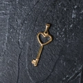 Detailed macro view of a vintage gold heart key pendant on a dark slate stone surface - H05 Heart Key