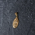 Detail of gold-plated oval Virgin Mary pendant on dark textured stone surface - H12 Virgin Mary Medal