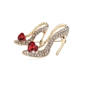Golden high heel brooch with white rhinestones and red heart shaped gems on a white background - Gold