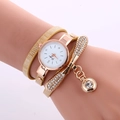 Close-up of golden wrap-around watch with rhinestone bow and sparkling pendant on wrist - Beige