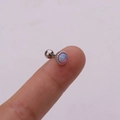 Close-up of small round opal cartilage earring with screw ball back in silver setting - Purple