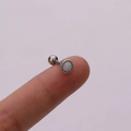 Macro shot of silver stainless steel opal stud earring held on a fingertip - White