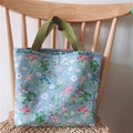 Floral cotton lunch bag with blue flower pattern and green handles on a wooden chair - Green with Floral Print
