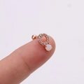 Gros plan d'un piercing d'oreille en or rose avec opale et détails en zircon - Opale Ronde Incrustée / Or rose