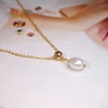 Collana in titanio dorato con ciondolo a perla d'acqua dolce su sfondo di rivista di moda - Stile Perla Bianca 8mm