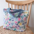 Detailaufnahme der Blumen-Stofftasche mit blauen Tragegriffen auf Korbstuhl - Rosa und blaue Blumen