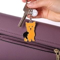 Detailansicht eines orange-schwarzen Terrier-Schlüsselanhängers an einer lila Ledertasche - Yorkie