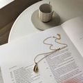 Elegante collar con colgante de concha en plata 925 dorada sobre un libro abierto - Collar de Concha / Oro de 18K